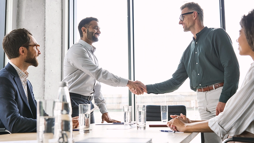 meeting personen schreibtisch haendereichen wasserglas Handschlag zwischen B2B-Partnern