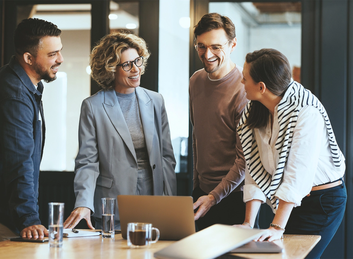 4 Personen diskutieren am Arbeitsplatz hinter einem Laptop