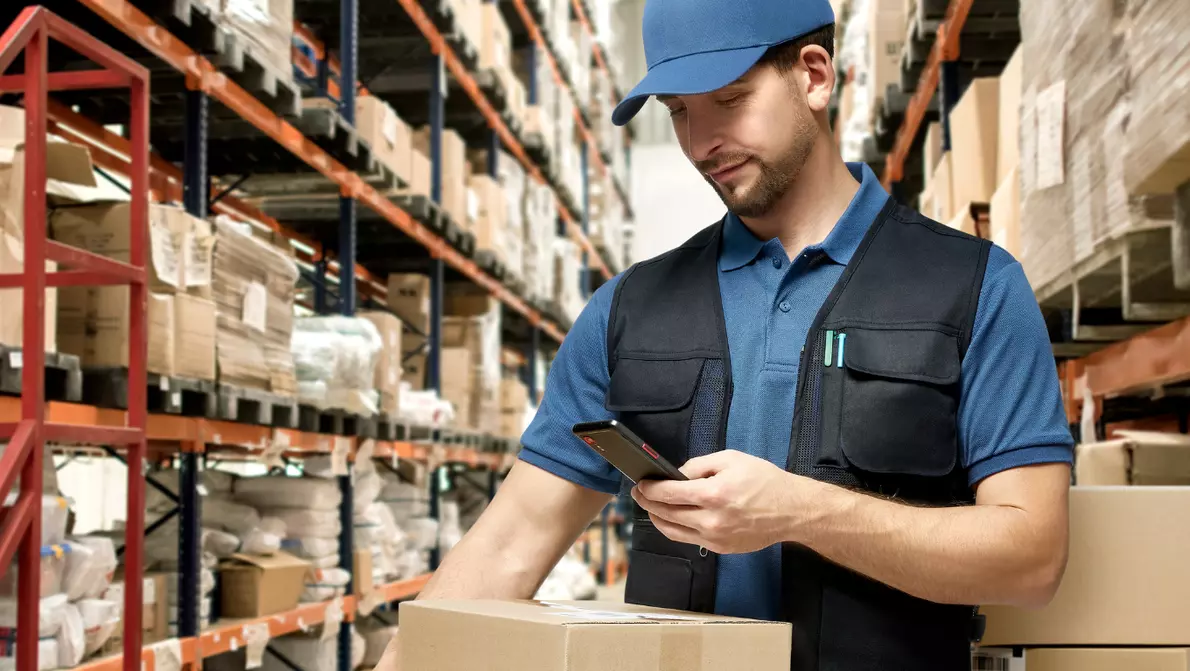 Samsung Smartphone in Transport und Logistik Mitarbeiter mit blauen Basecap nutzt Smartphone im Lager